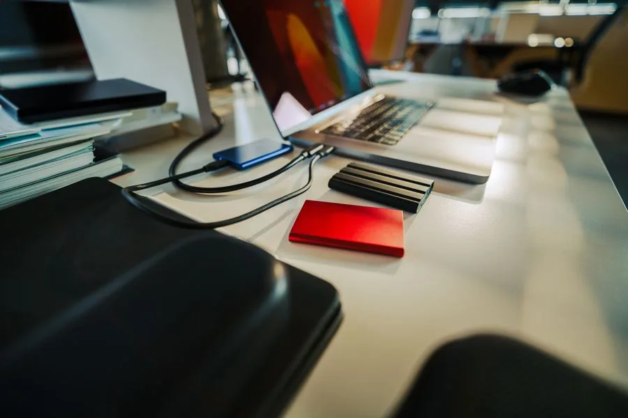 Mesa de trabalho com HDs externos e SSDs portáteis conectados a um notebook